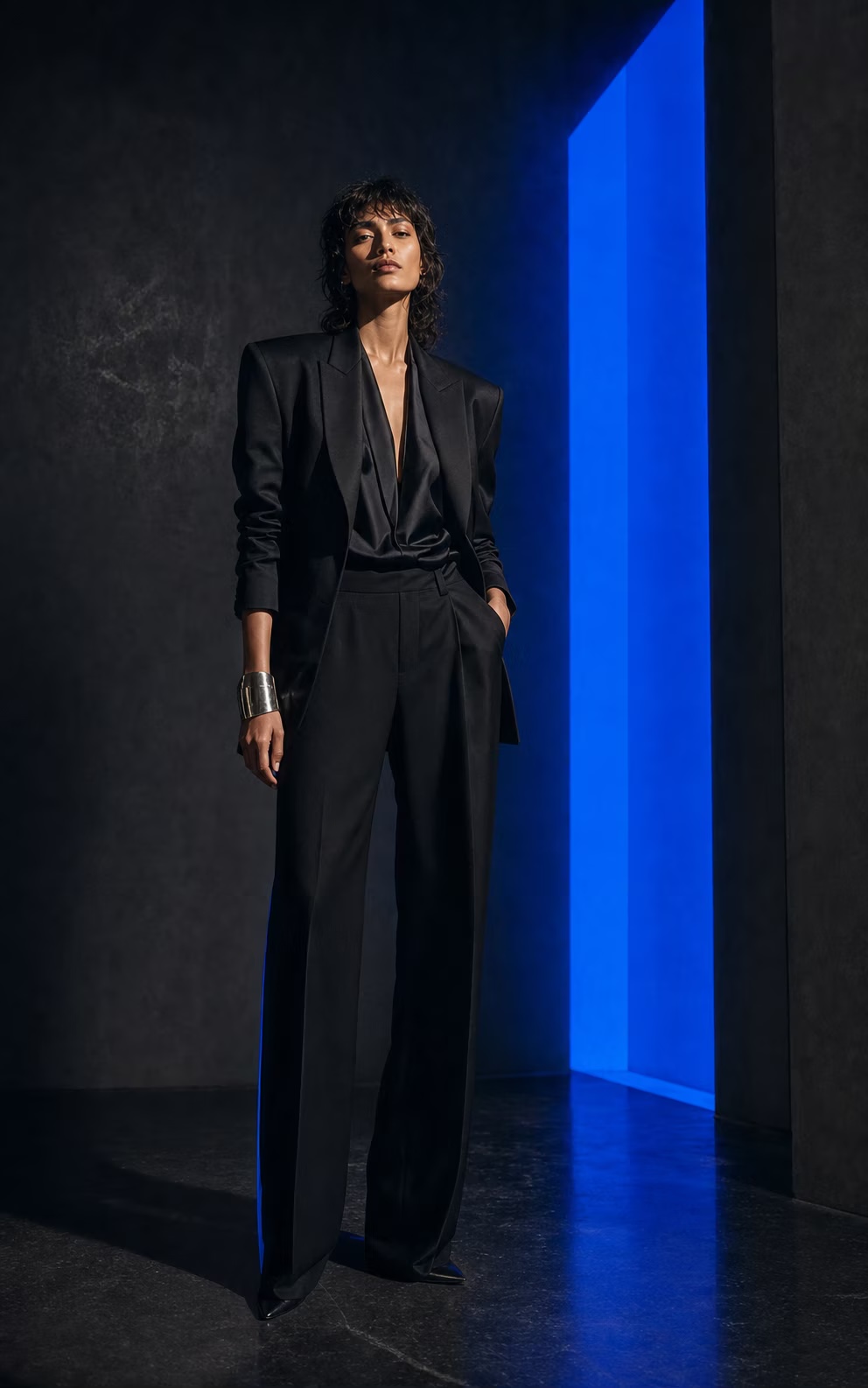 Model in a black evening suit beside a cobalt doorway of light.