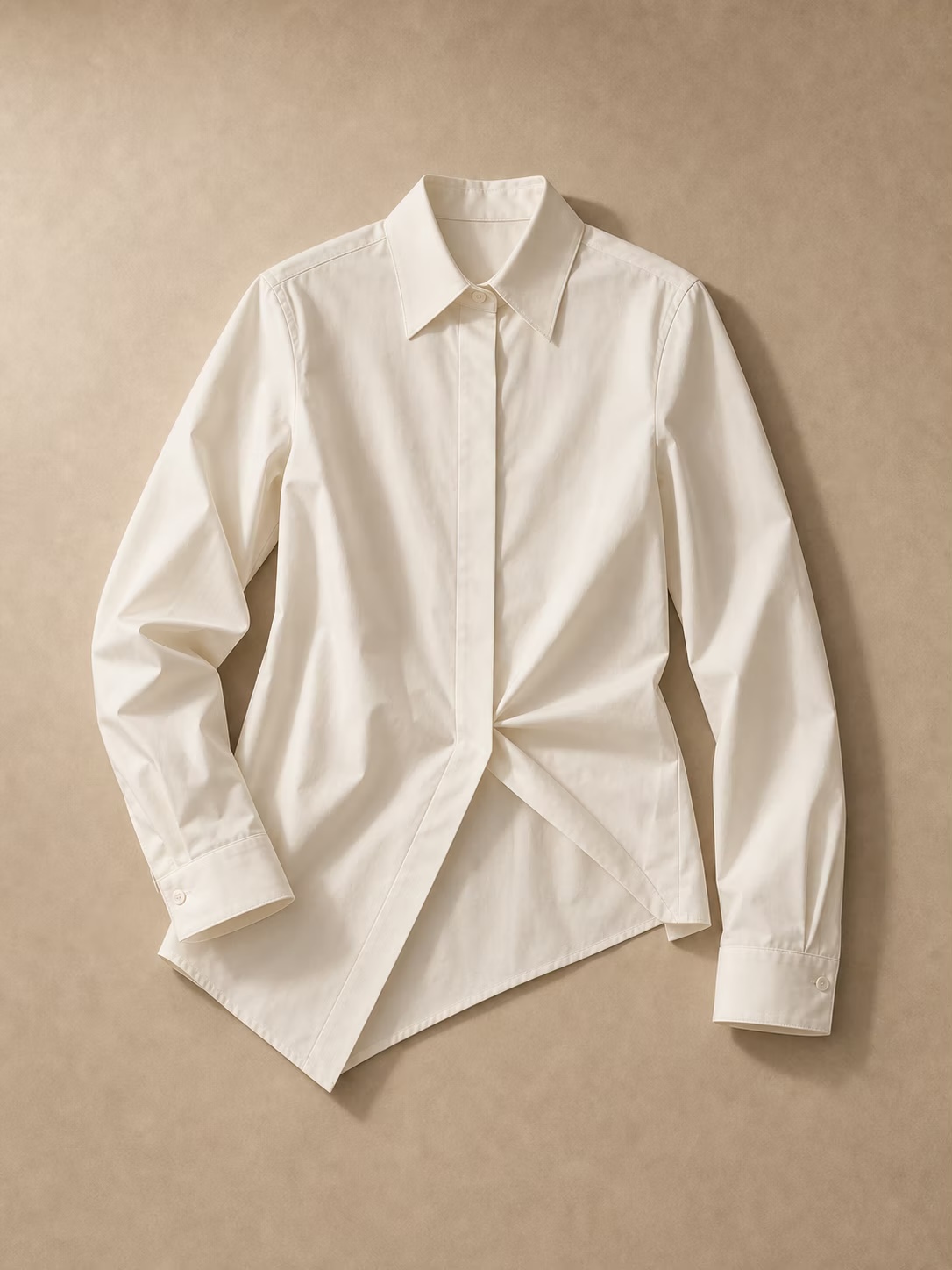 Ivory asymmetric shirt photographed on a warm chalk background.